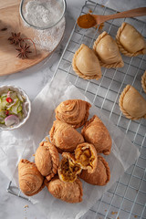 Traditional curry puffs stuffed chicken with raw curry puffs on table as background