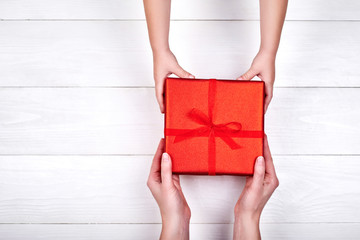 Son giving red gift box to mum, copy space. Child and mother hands with gift on white background....