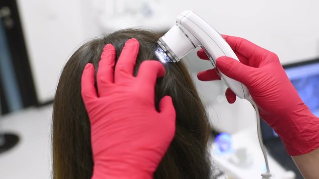 doctor dermatologist diagnoses the structure of the hair of a young pretty girl with a special tool - a trichoscope. Trichology, trichogram