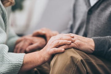 cropped view of retired couple holding hands - Powered by Adobe