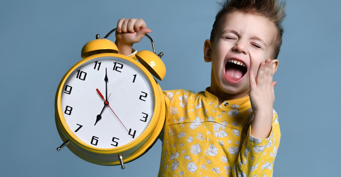 Cute Little Boy With Alarm Clock,isolated On Blue. Funny Kid Pointing At Alarm Clock At 7 O'clock At Morning.