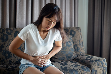 asian woman suffering from abdominal pain while sitting at home