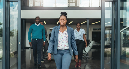 Confident african business woman wallking out of the office with coleagues behind her