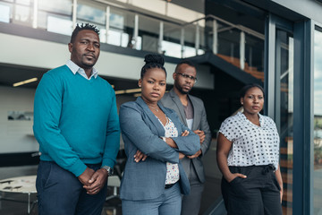 Portrait of a confident black businesswoman crossing her arms with all african team in the background