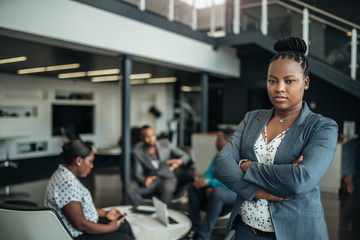 Obraz na płótnie Canvas Portrait of a confident black businesswoman with her arms crossed and all african team in the background