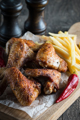 Barbecue grilled chicken wings close up with fries, tomato ketchup sauce and beer on wooden background. Meat food concept. 