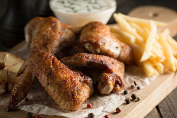 Barbecue grilled chicken wings close up with fries, tomato ketchup sauce and beer on wooden background. Meat food concept. 