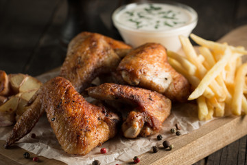 Barbecue grilled chicken wings close up with fries, tomato ketchup sauce and beer on wooden background. Meat food concept. 