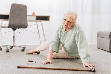helpless retired woman with blonde hair sitting on floor at home