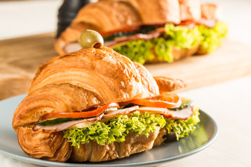 Photo of tasty and fresh croissant sandwich with salad, ham, cheese, tomatoes on wooden background. Morning breakfast concept. Healthy and fast food.