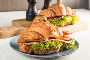 Photo of tasty and fresh croissant sandwich with salad, ham, cheese, tomatoes on wooden background. Morning breakfast concept. Healthy and fast food.