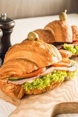 Photo of tasty and fresh croissant sandwich with salad, ham, cheese, tomatoes on wooden background. Morning breakfast concept. Healthy and fast food.