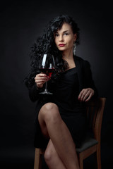 Fototapeta na wymiar Portrait of attractive brunette with glass of wine on a black bacground.