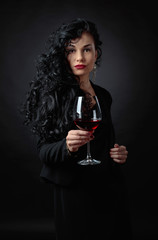 Portrait of attractive brunette with glass of wine on a black bacground.