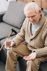 senior man holding pills and glass of water and looking at hand