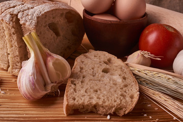 fresh delicious bread, concept for baking. Eggs in clay bowl, garlik, tomato and wheat sprouts on wooden table
