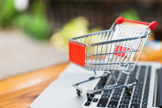 Empty Shopping cart on table with laptop keyboard and copy space for online shopping concept