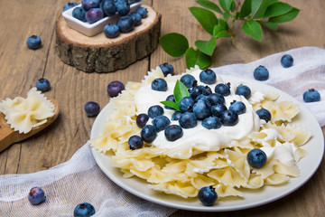 Tasty pasta with fresh organic blueberries and vanilla cream. Sweet dinner on retro wooden table.