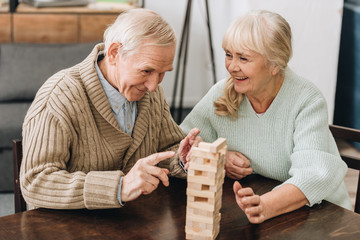 cheerful retired husband and wife playing jenga game on table