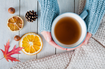 Woman in a warm knit sweater holds a cup of tea in hands on a wooden table