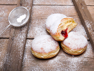 Tradycyjne pączki z cukrem pudrem i nadzieniem na drewnianym tle. Smaczne pączki z dżemem  © czarny_bez