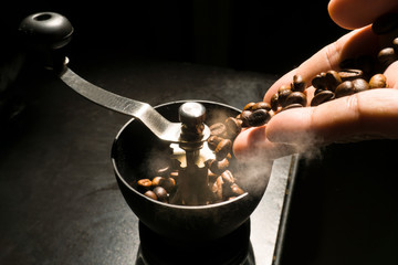 Hand pour coffee beans into grinder with smoke, isolated on coffee drink maker concept.