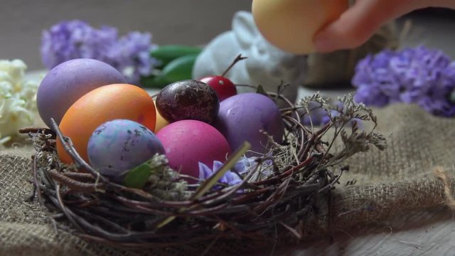 Child's hand takes and lays festive colored egg in in the Easter nest