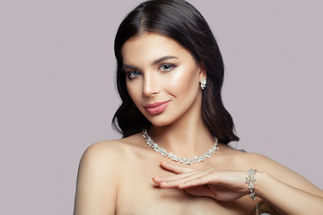 Young smiling woman with makeup and diamond necklace, bracelet and earrings on pink background