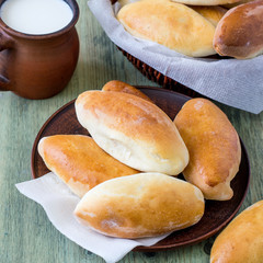 Homemade ruddy pies with filling on a round plate and in a wicker basket, next to a mug of milk.
