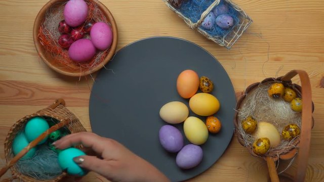 Woman's hand puts colored festive easter eggs in grey plate from different baskets
