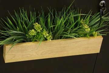 long wooden brown pot with decorative green grass and flowers on the wall in the room