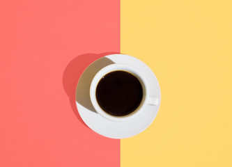 White cup of freshly brewed coffee with saucer on trendy duotone living coral pastel sand color background. Top view. Morning energy fashion female business concept. Minimalist style. Pop Art 80s