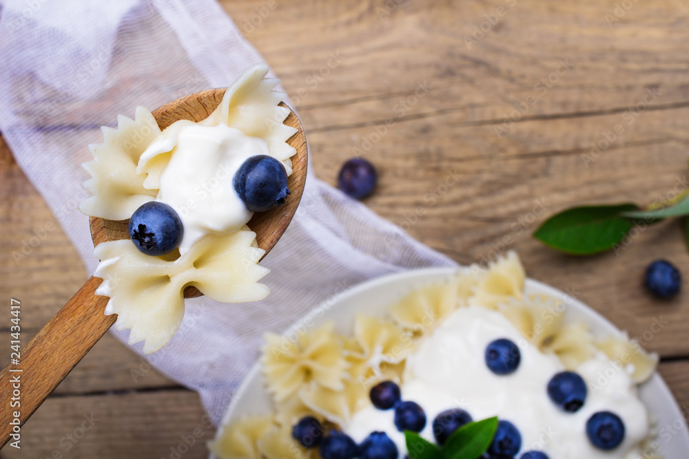 Wall mural Tasty pasta with fresh organic blueberries and vanilla cream. Sweet dinner on retro wooden table.