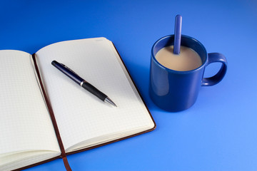 Open a blank white notebook, pen and cup of tea on the blue desk