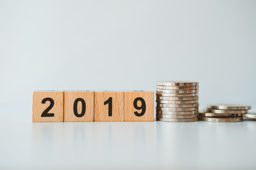 Wooden block year 2019 with stack coins on grey background using as business and finance concept