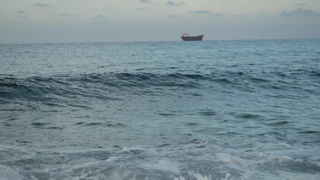 Small freight ship sail by the sea, waves cover the stone, splash and create foam