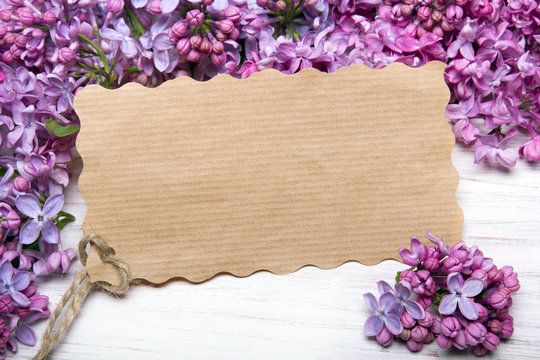 Lilac flowers and empyt card on white wooden background, copy space