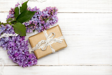 Fototapeta na wymiar Lilac flowers, gift box on white wooden background, copy space