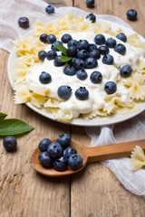 Tasty pasta with fresh organic blueberries and vanilla cream. Sweet dinner on retro wooden table.