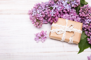 Lilac flowers and gift box on white wooden background, copy space