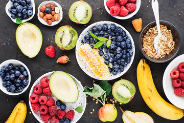 Ingredients of a healthy breakfast: raspberries, blueberries, oat flakes, granola, honey, nuts, banana, avocado kiwi on the background Top View