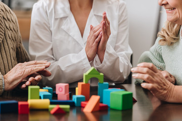 cropped view of female caregiver applauding to senior couple while playing with wooden toys