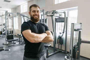 Fototapeta na wymiar Smiling positive confident male personal instructor with arms crossed in fitness gym