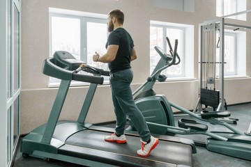 Fototapeta premium Athletic muscular bearded man running on treadmills in modern sport gym. Fitness, sport, training, people concept