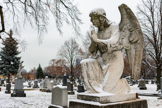 Praying Angel on top of a Tombstone at a Cemetery in Winter with Snow