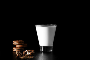 Glass of milk and chocolate cookies on black background