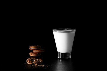 Glass of milk and chocolate cookies on black background