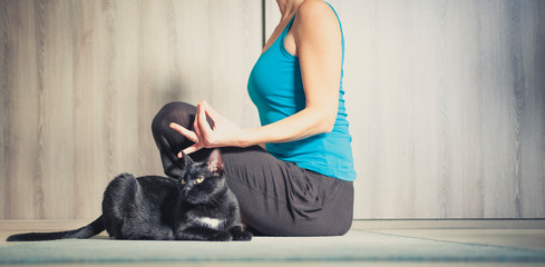woman doing yoga at home - black cat sitting next to her