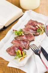 slices of roast beef medium rare with greens on wooden table