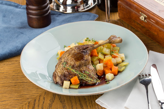 Roasted duck leg with vegetable stew in blue plate on wooden table Restaurant menu